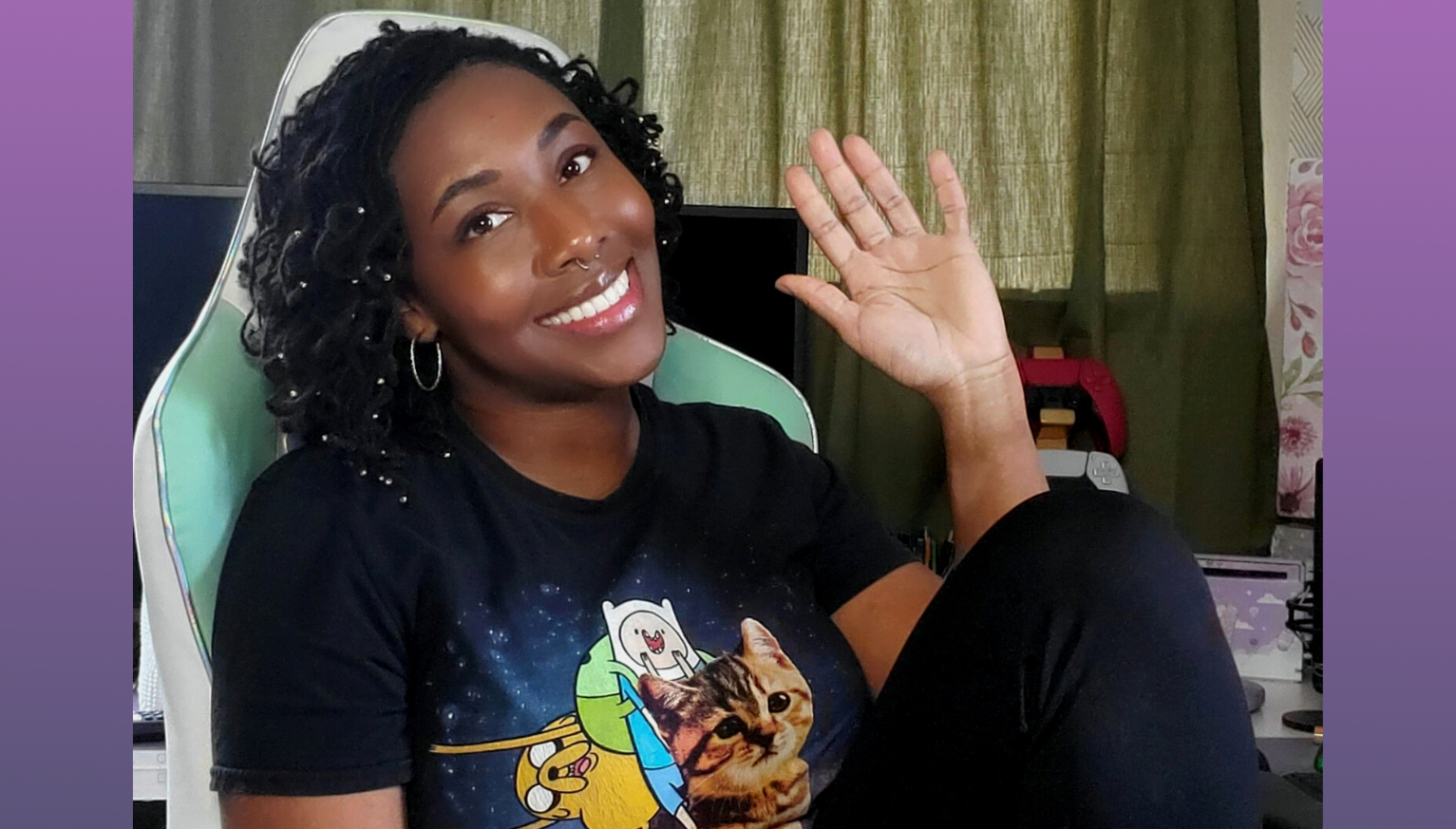 Jasmine Taylor at her desk smiling, waving, and wearing an Adventure Time t-shirt